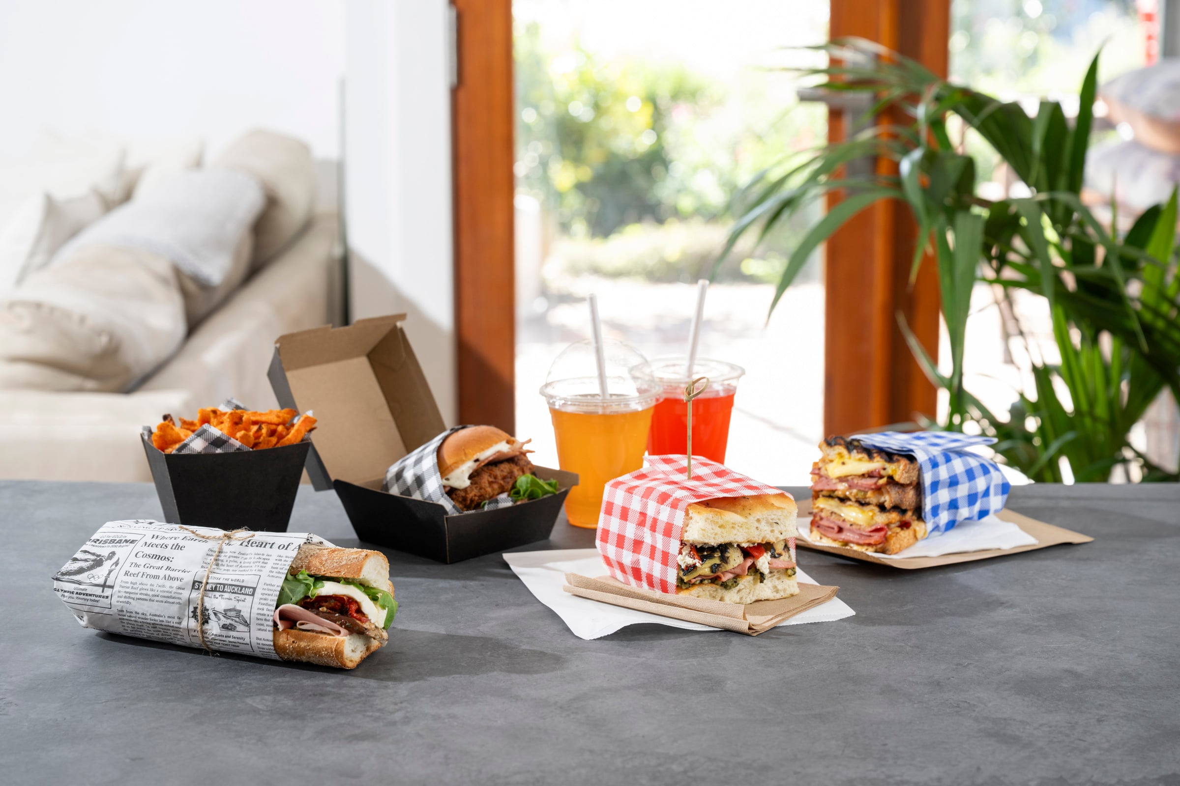 Detpak Greaseproof Wrap dispenser with black gingham paper, next to sandwiches and fries in colored gingham wraps.