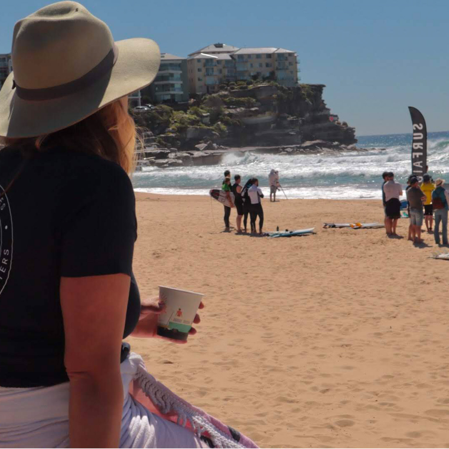 Image of person drinking from a RecycleMe™ cup while sitting on the beach