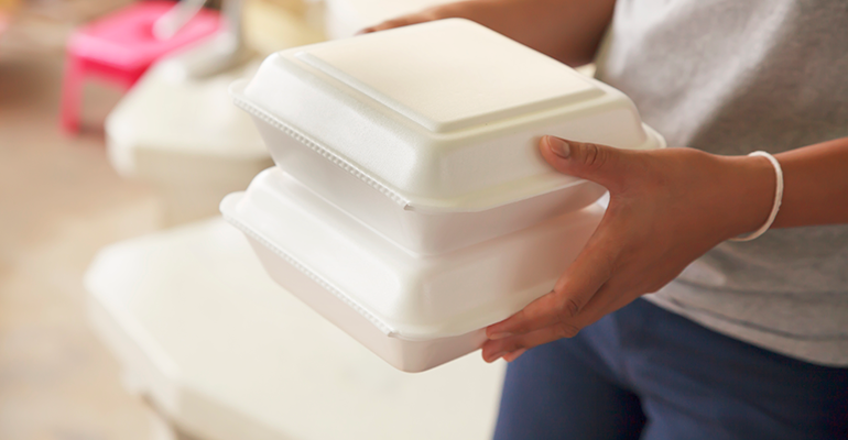 Woman carrying a pile of polystyrene food clamshells.